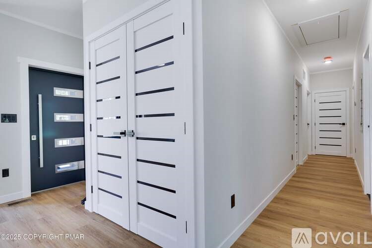 A hallway with white walls and wooden floors leading to a black door.