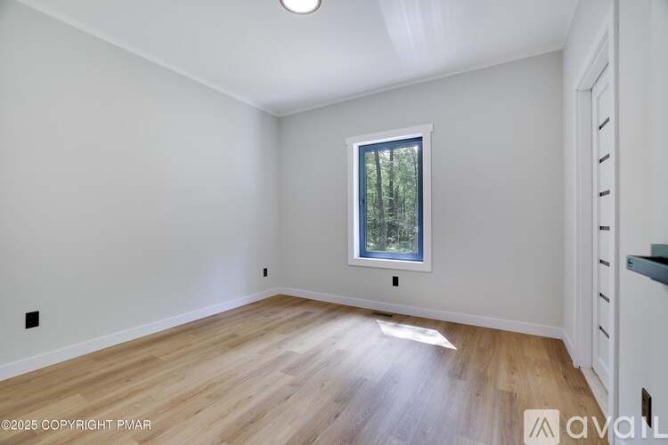 A room with wooden flooring and a window showing trees outside.
