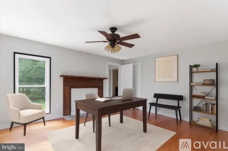 A room with a fireplace, a chair, a table, and a fan.