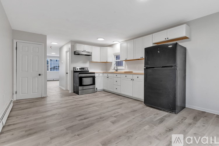 A kitchen with a black fridge, white cabinets, and wooden floors.