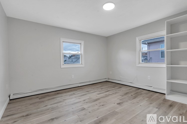A room with wooden flooring and a window showing a house in the distance.