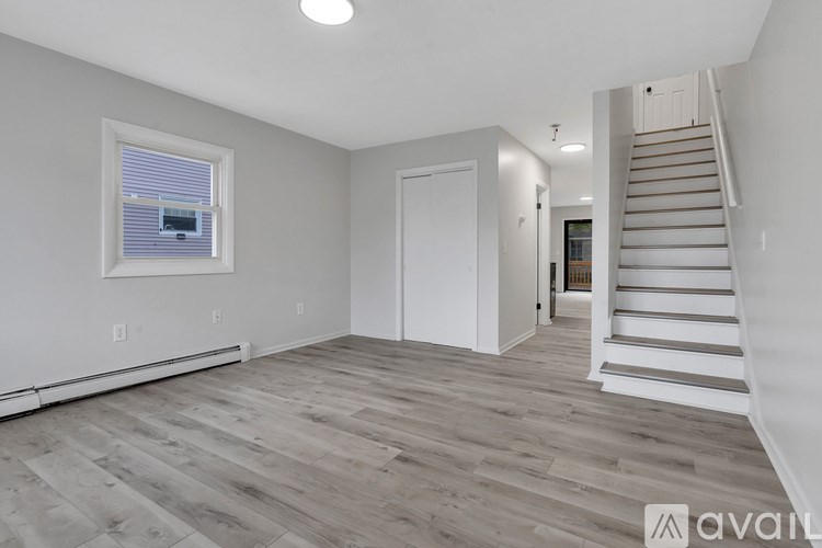 A spacious room with wooden flooring and a staircase leading to another room.