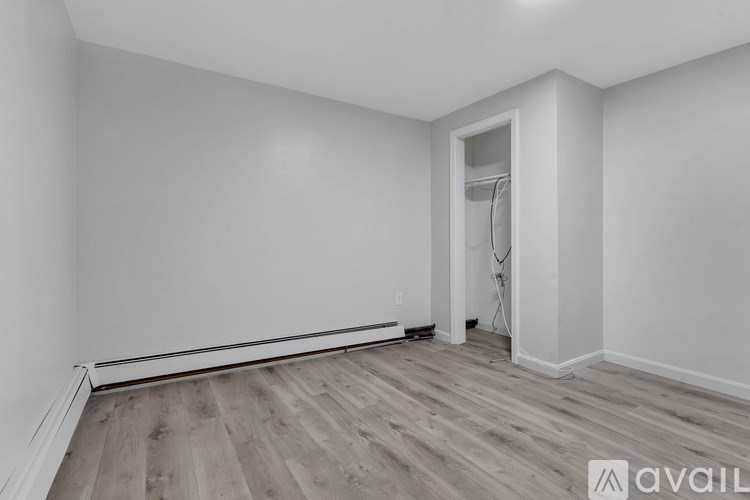 A room with a wooden floor and white walls, with a doorway leading to another room.