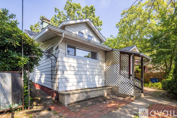 A house with a white exterior and a brown roof is surrounded by greenery.