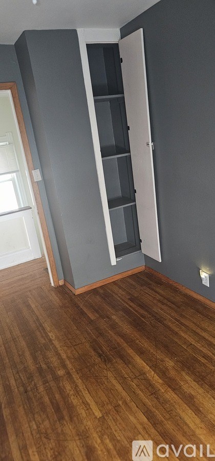 A room with a wooden floor and a grey wall with a white door.