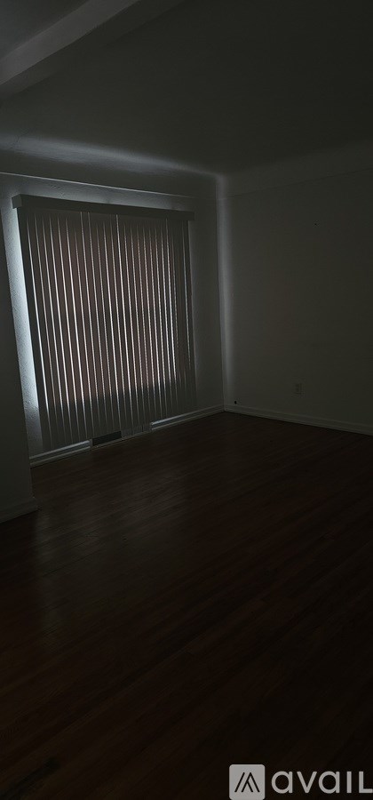 A room with wooden flooring and a window with blinds.