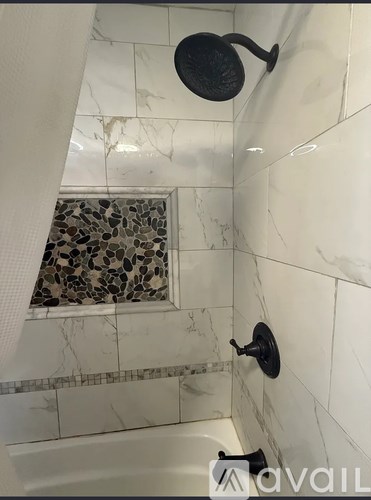A bathroom with a shower head and a marble tile shower area.