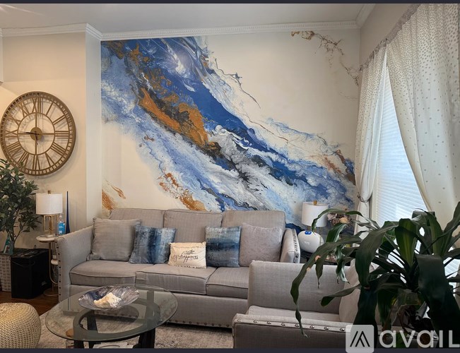 A living room with a grey couch and a large painting on the wall.