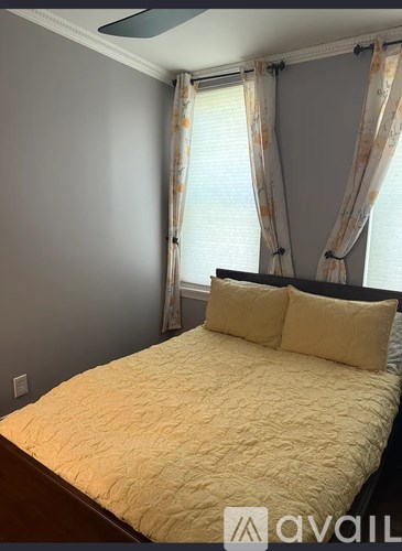 A bed with a yellow comforter and two pillows sits in a room with a window covered by curtains.