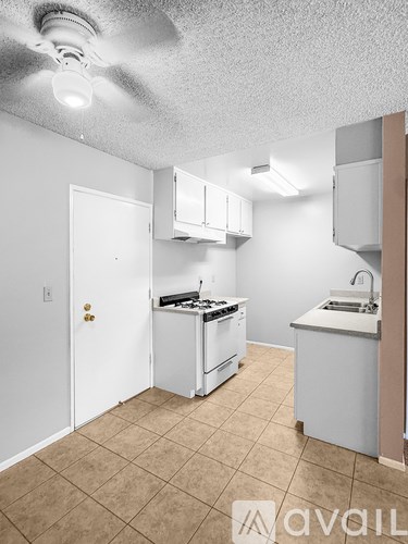 A small, empty kitchen with white appliances and a beige tile floor.