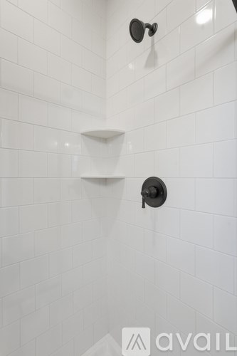 A white tiled shower with a black faucet.