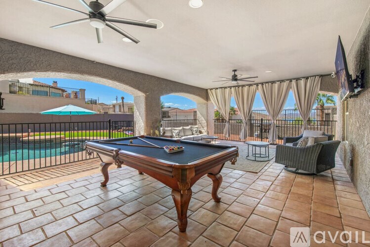 A pool table is in the middle of a patio with a pool table fan and a television.