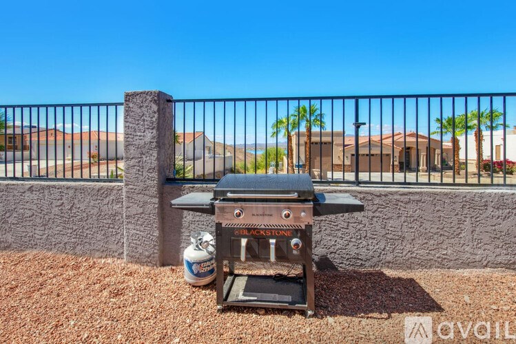 A grill is on a gravel area in front of a fence.