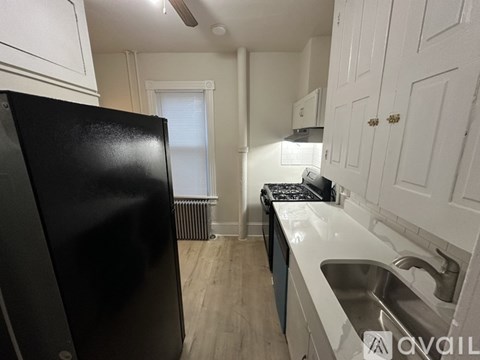 A black refrigerator stands in a kitchen with white cabinets and a stove.
