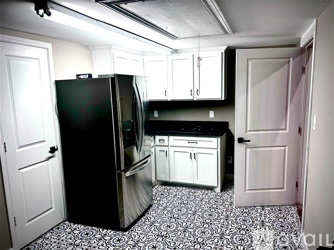 A black fridge in a kitchen with white cabinets and a black and white floor.