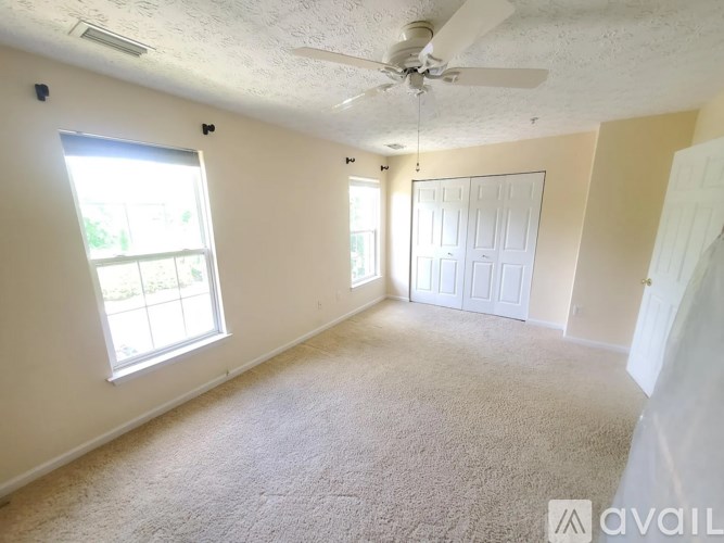 A room with a carpeted floor, a ceiling fan, and a window with blinds.