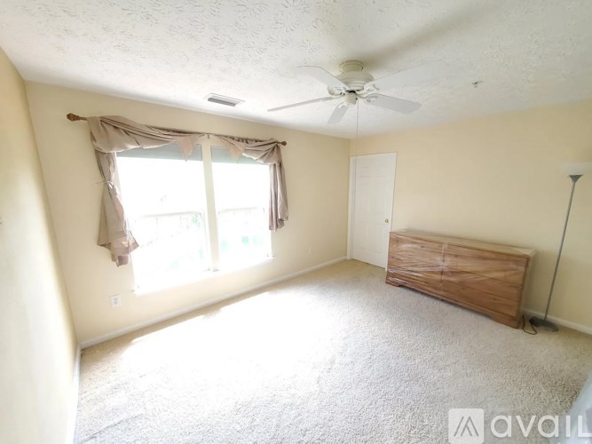 A room with a ceiling fan, carpeted floor, and a window with curtains.