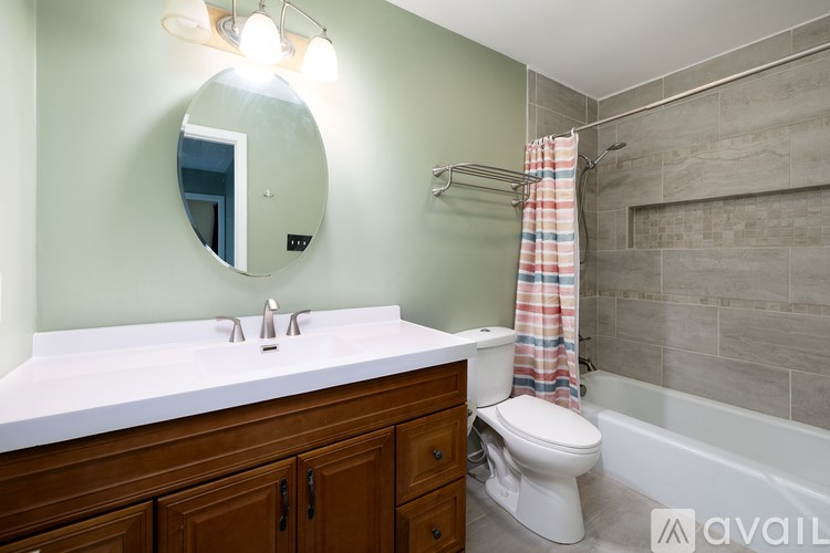 A bathroom with a white countertop, a round mirror, a white toilet, and a shower with a striped shower curtain.