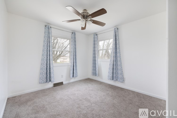A room with a ceiling fan and two windows with curtains.