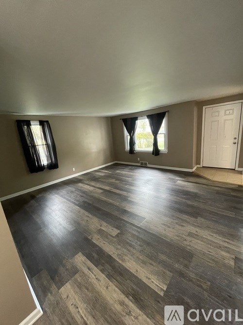 A room with a wooden floor and a window with curtains.