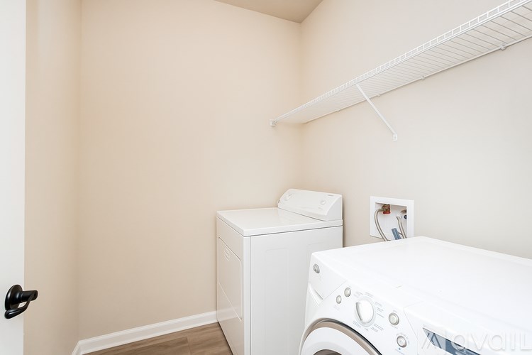 A white washing machine sits in a laundry room with a white shelf above it.