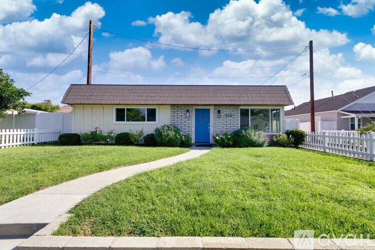 A small house with a blue door is surrounded by a white picket fence.
