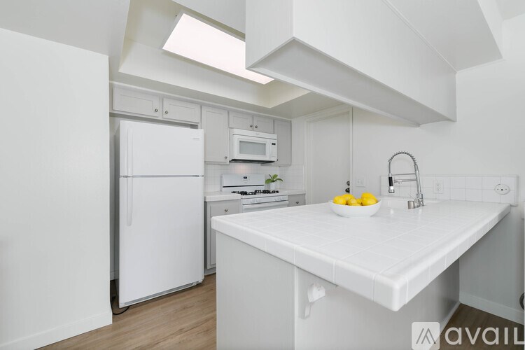 A white kitchen with a refrigerator, microwave, and sink.