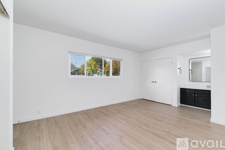 A spacious room with wooden flooring and a large window showing an outdoor view.