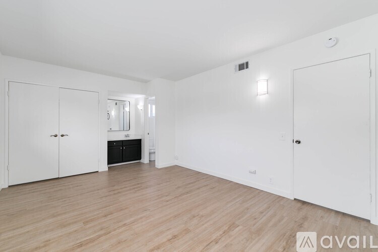 A room with white walls and wooden flooring, with a white cabinet and a black appliance in the corner.