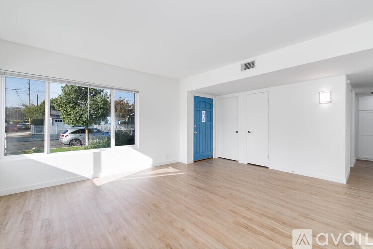 A room with wooden floors and white walls, a blue door, and a window showing an outdoor scene.