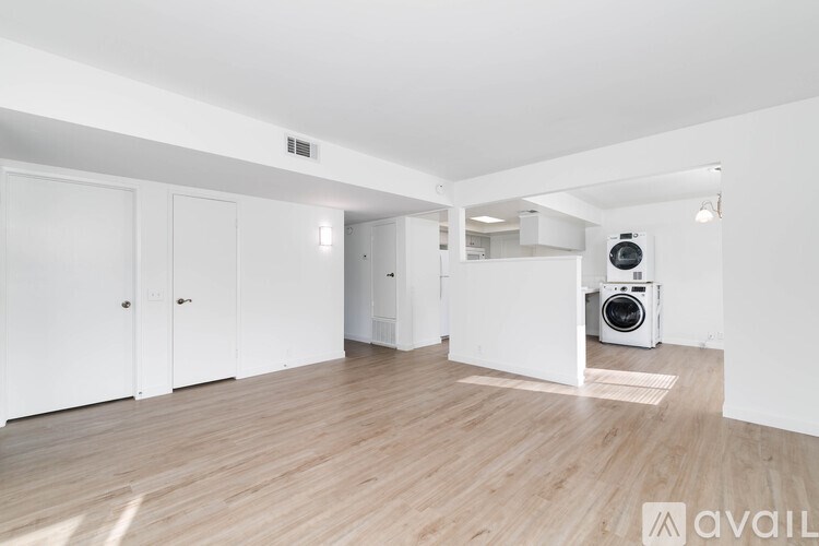 A room with wooden flooring and white walls, with a white cabinet and a white fridge.