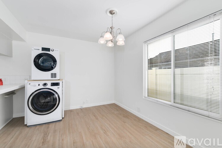 A white washing machine is stacked on top of another in a room with a window and blinds.