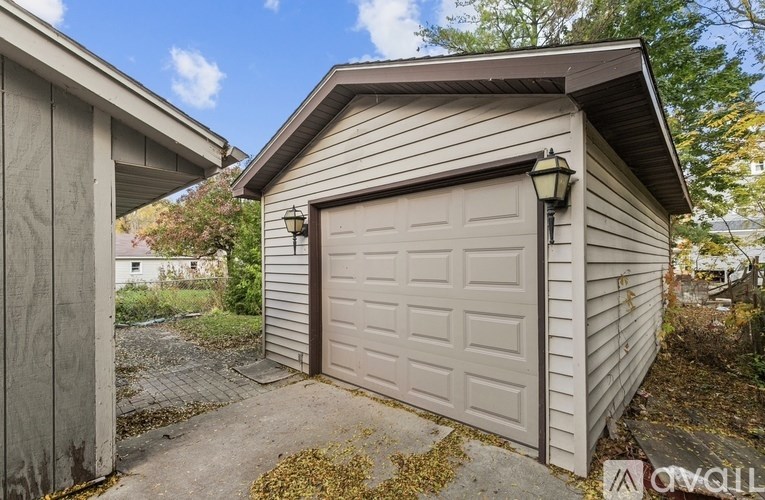A small garage with a closed door is situated next to a house.
