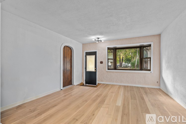 A room with wooden flooring and a window with a view of trees.