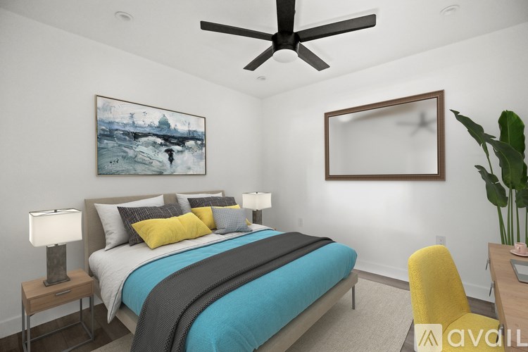 A bedroom with a bed, a ceiling fan, a painting, a mirror, and a plant.