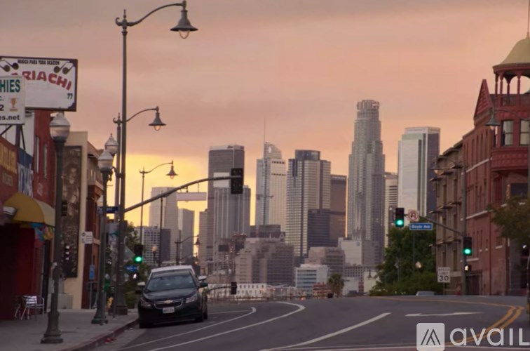 A city street with a car driving down the road and tall buildings in the background.