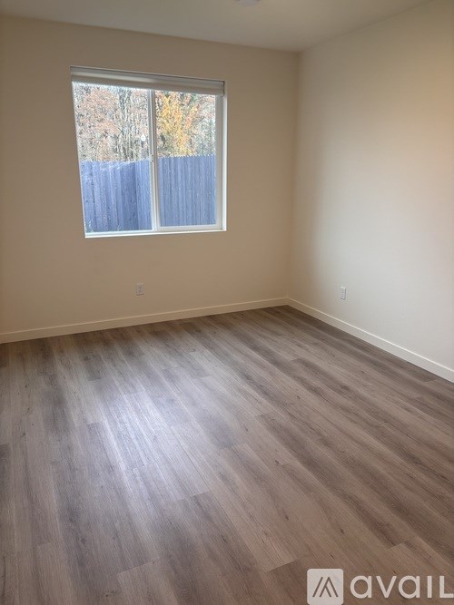 A room with wooden flooring and a window with a view of a fence and trees.