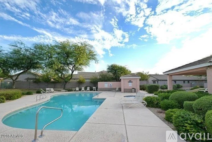 A pool surrounded by a concrete patio and a small building.