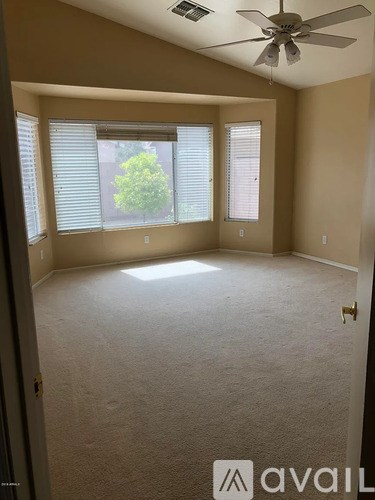 A room with a carpeted floor, a ceiling fan, and a door leading to a balcony with a tree visible outside.