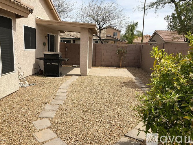 A backyard with a gravel patio and a BBQ grill.