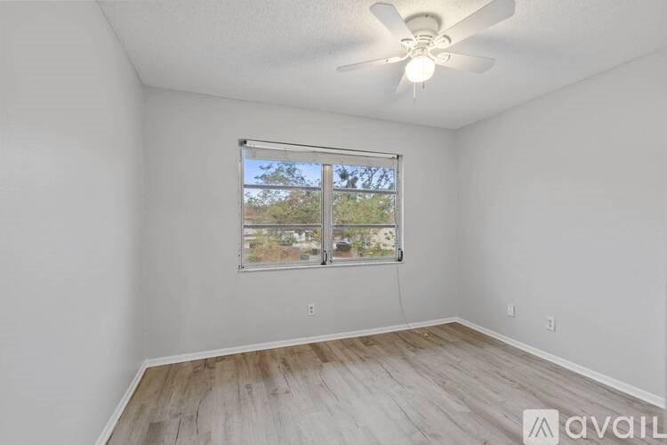 A room with a ceiling fan and a window showing a view of trees and houses outside.