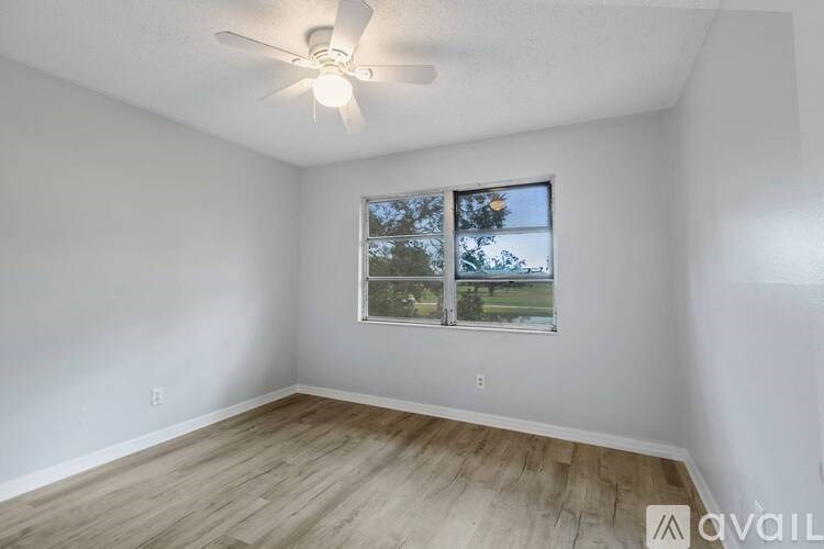 A room with a ceiling fan and a window showing trees and a bridge outside.