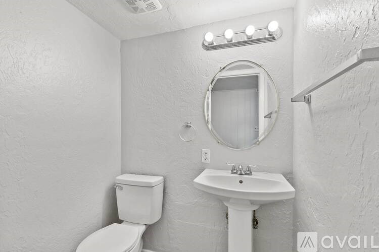 A bathroom with a toilet, sink, mirror, and lights.