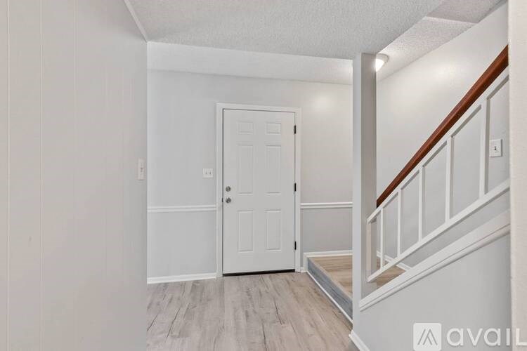 A white door is in a hallway with a wooden staircase.