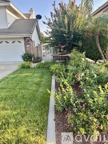 A well-maintained garden with a fountain and a house in the background.
