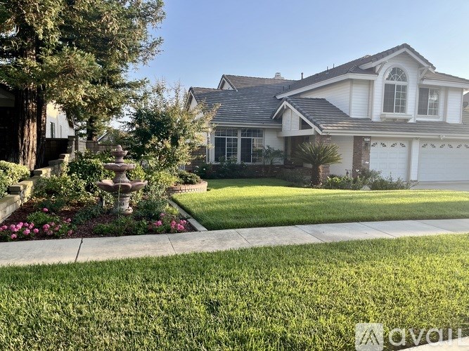 A white house with a grey roof and a fountain in the front yard.