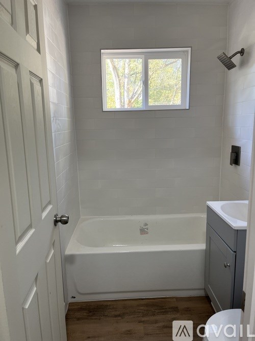 A white bathroom with a tub, sink, and window.