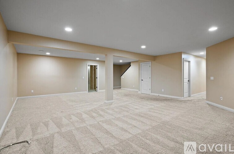 A spacious room with a carpeted floor and a staircase in the background.