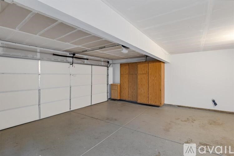 A spacious garage with a white ceiling and a white wall with a wooden cabinet.