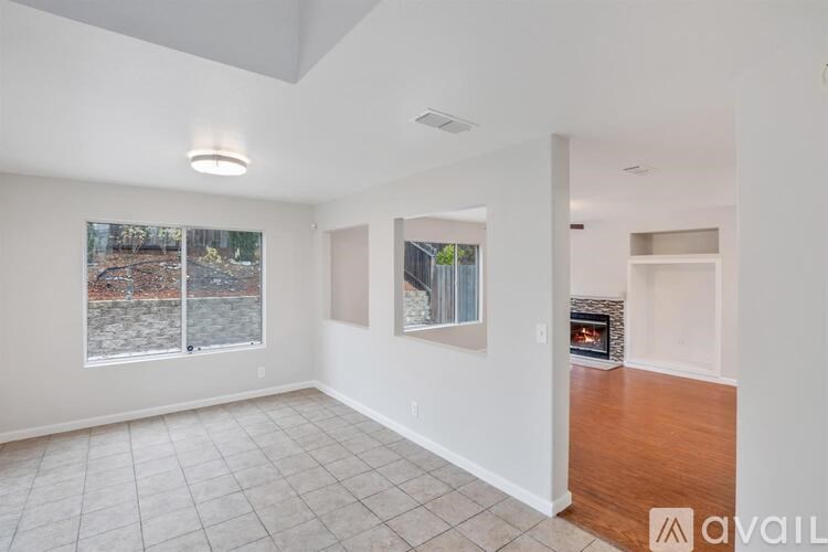 A spacious living room with a fireplace and a view of a wooded area outside the window.